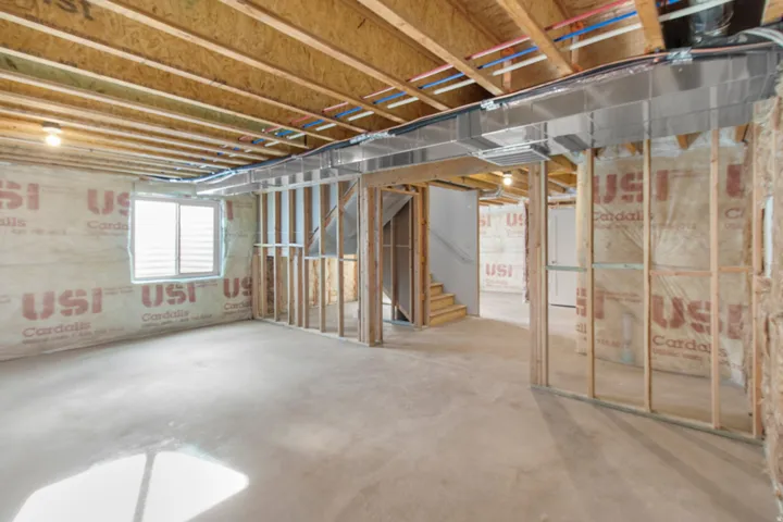 Unfinished lower level with wood framing, exposed ceiling joists, ductwork, and a window