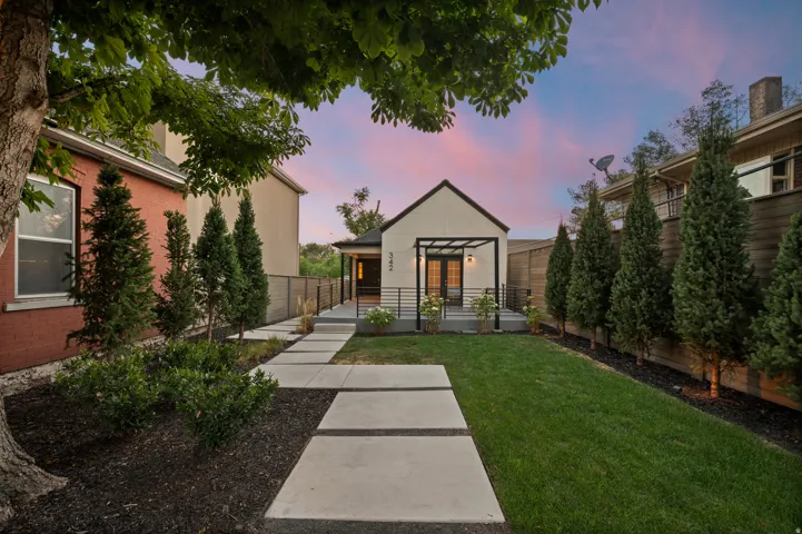 Manicured lawn with concrete paver pathway leading to a covered entry with dual doors