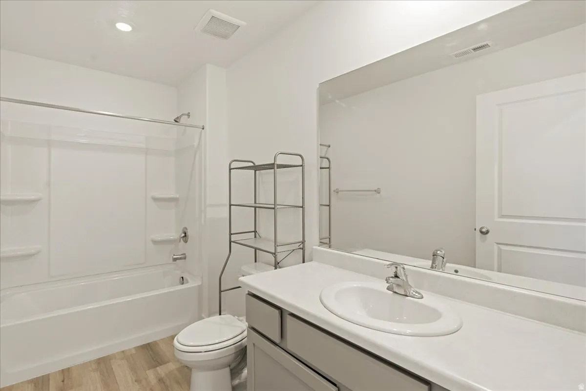 White tub-shower combination with integrated shelving, a single vanity with an integrated sink, a large mirror, and wood-finish flooring