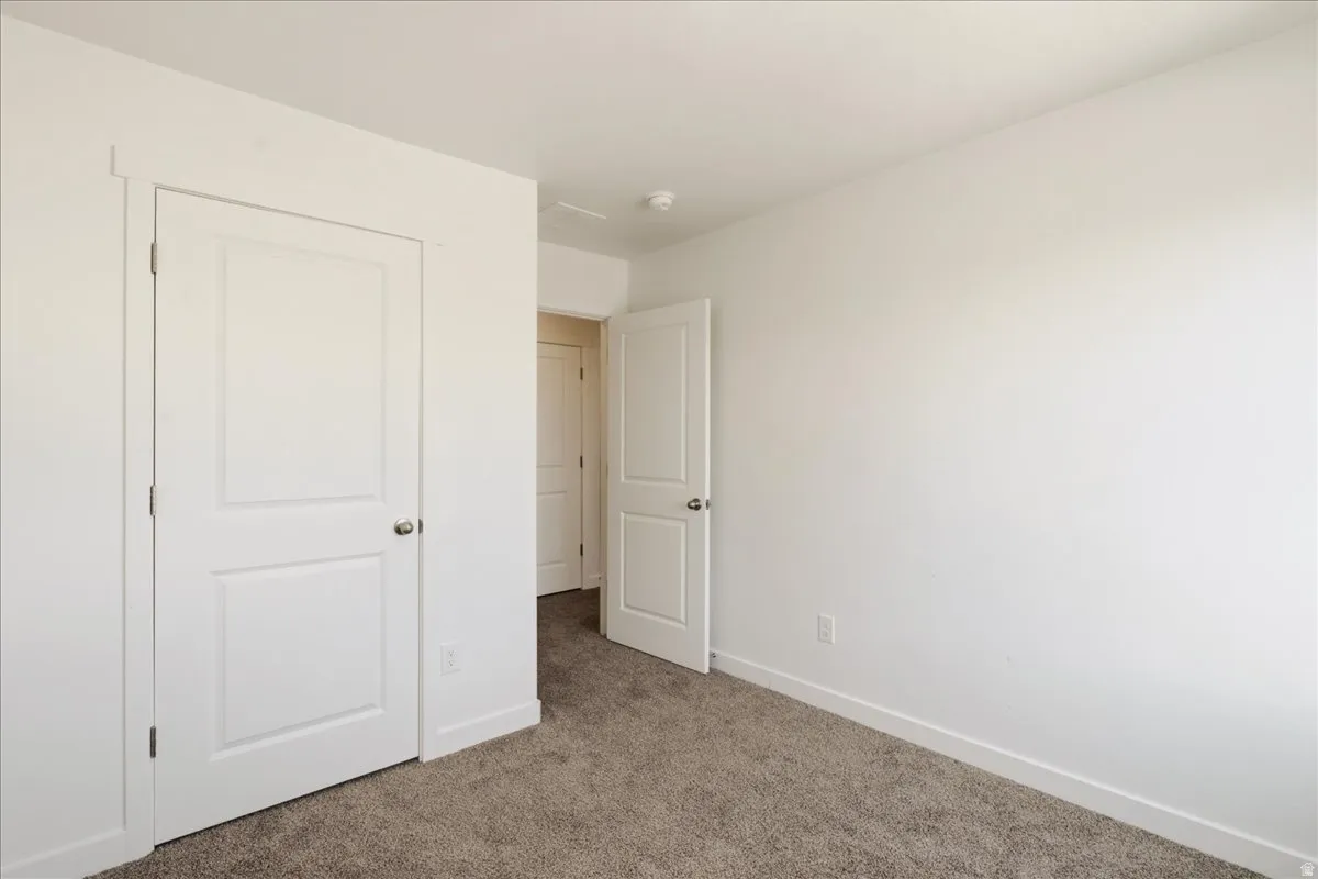Bright secondary bedroom featuring neutral carpet flooring, two white six-panel closet doors with hardware, and clean white walls with recessed ceiling lighting
