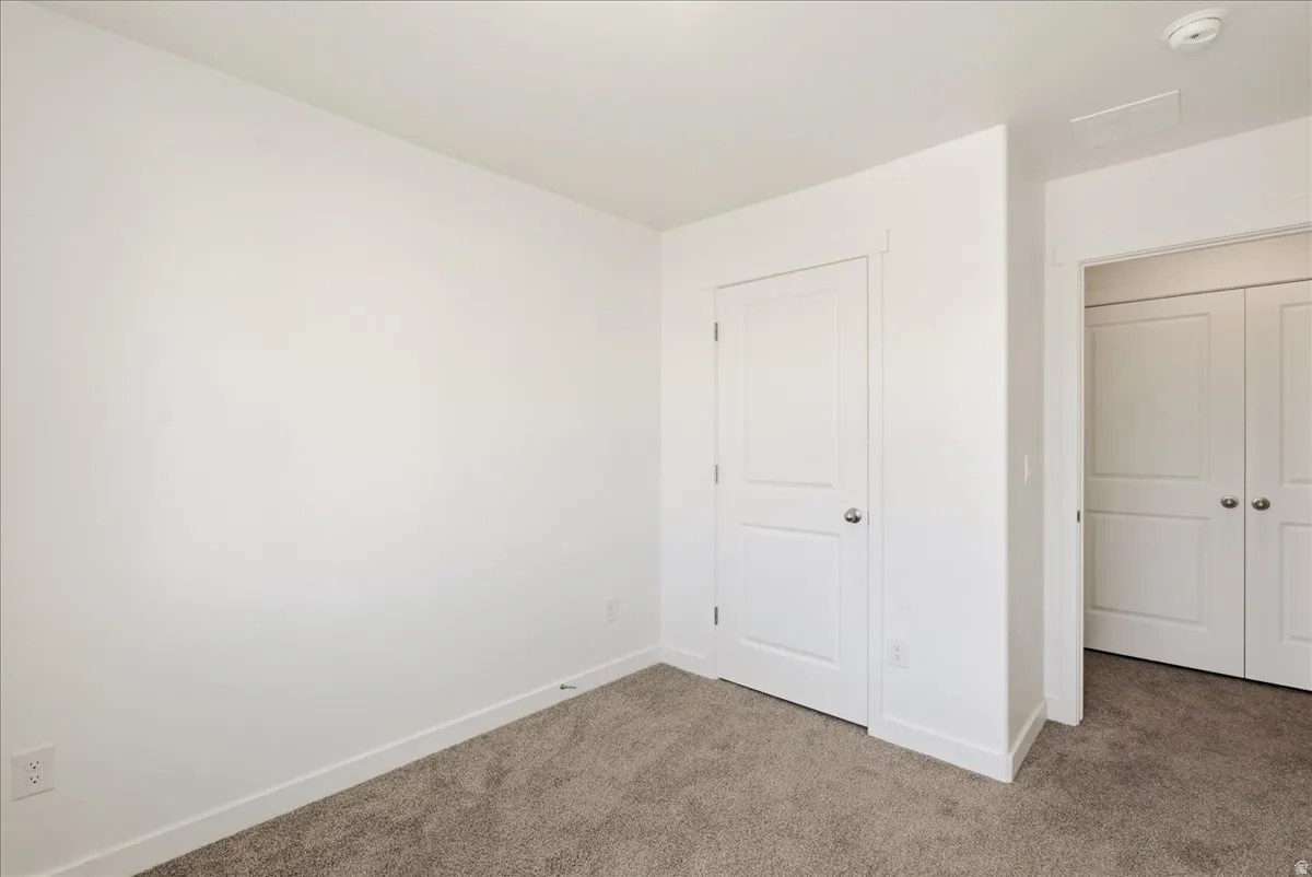 Neutral-toned carpeting paired with white walls, featuring a paneled door and bi-fold closet doors