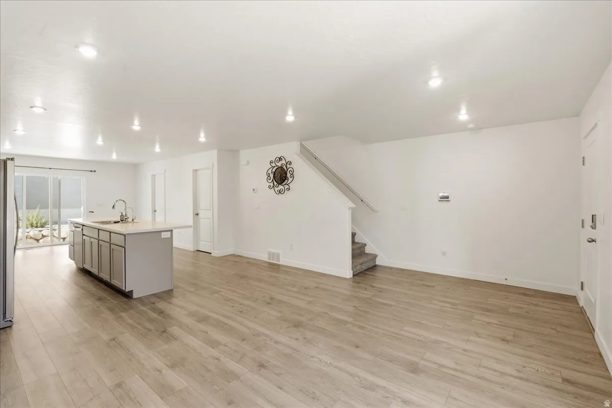 Open-concept living area featuring wood-finish flooring, recessed lighting, a kitchen island with seating, and sliding glass doors to the exterior