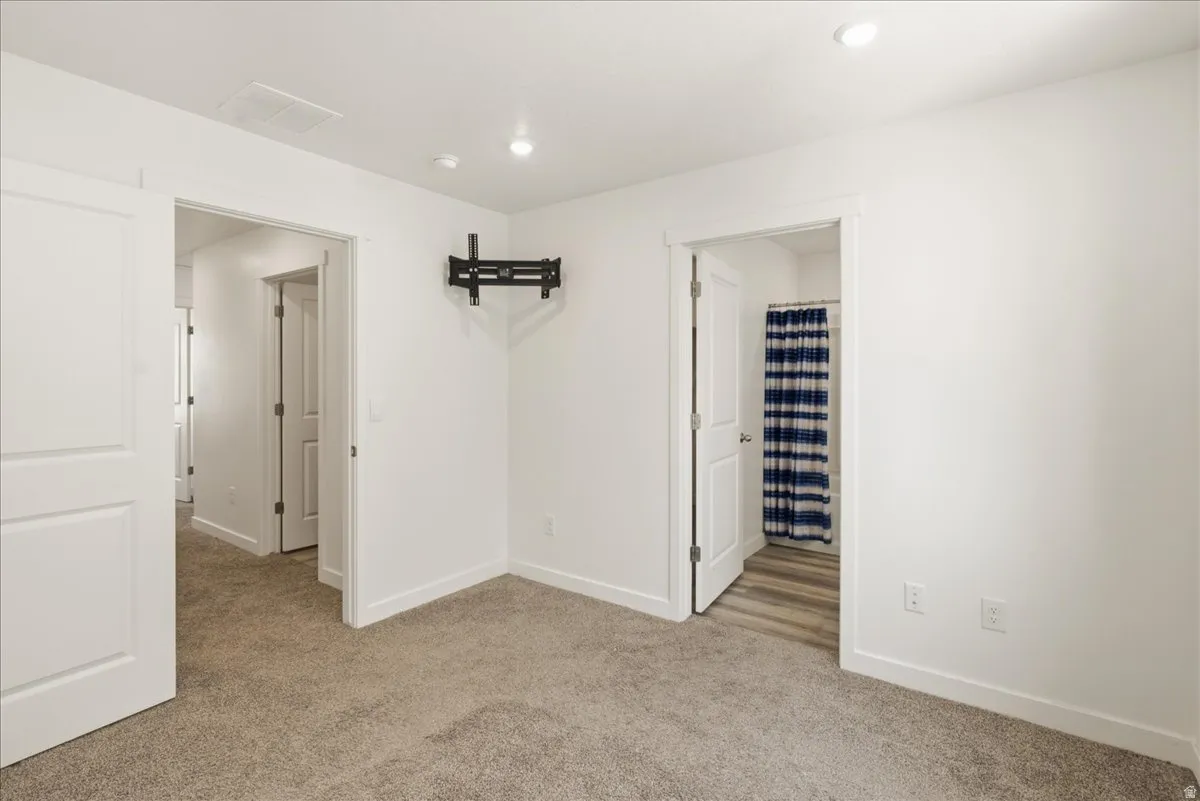 Wall-mounted television bracket, recessed ceiling lighting, and light gray carpeting