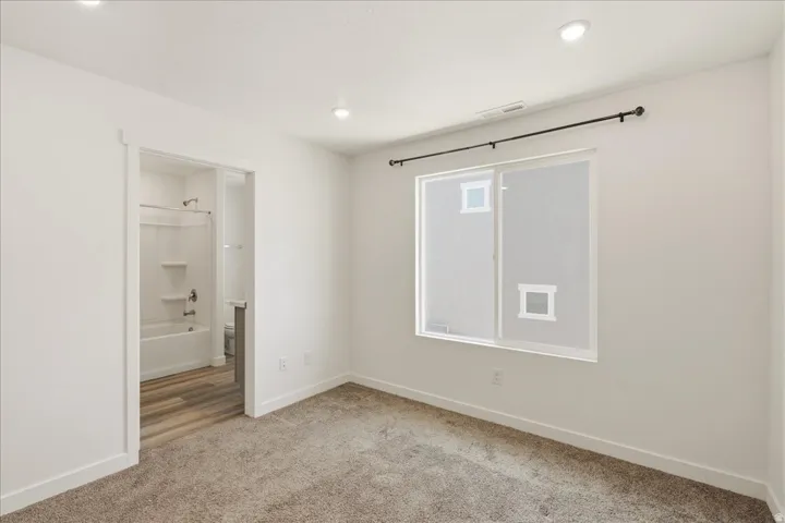 Carpeted room with recessed lighting and a sliding window, featuring a bathroom with wood-finish flooring and a bathtub