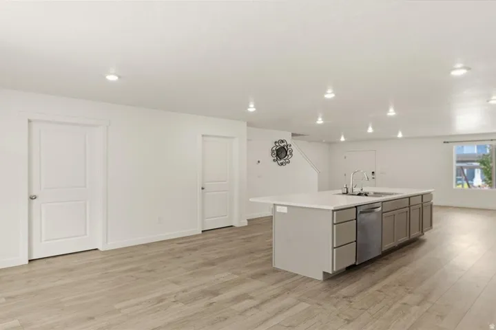 Spacious open-concept area featuring wood-finish flooring, recessed lighting, a large kitchen island with a sink and ample counter space, and light-toned cabinetry