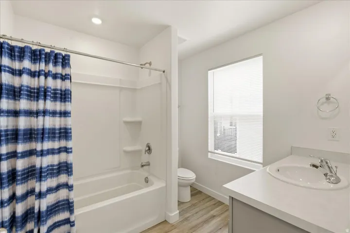 Bathroom featuring a white tub and shower combination, a single window with blinds, a vanity with an integrated sink, and wood-finish flooring