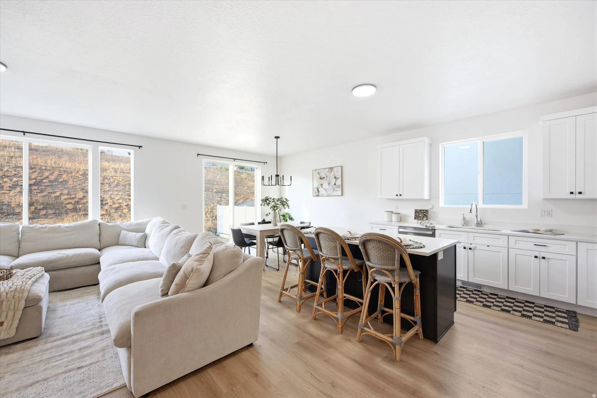 Open-concept living area with wood-finish flooring, white cabinetry, and a kitchen island with a light-colored countertop