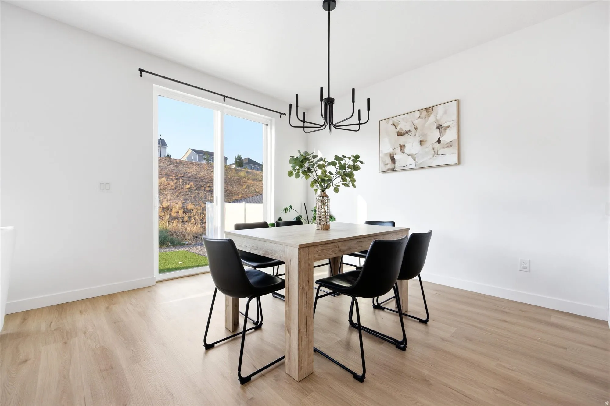 Sliding glass door leading to exterior, wood-finish flooring, and a modern black chandelier