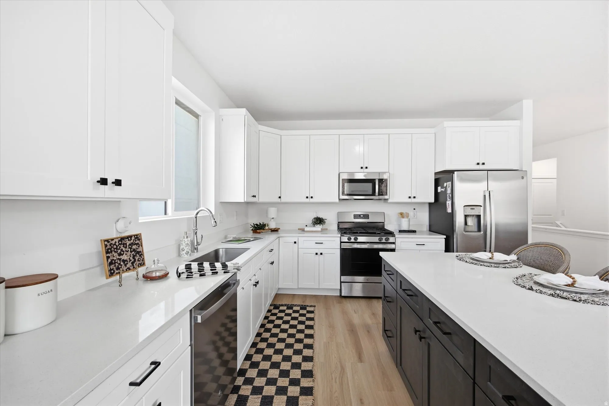 White shaker-style cabinetry, stainless steel appliances, wood-finish flooring, white countertops, and a contrasting island with seating