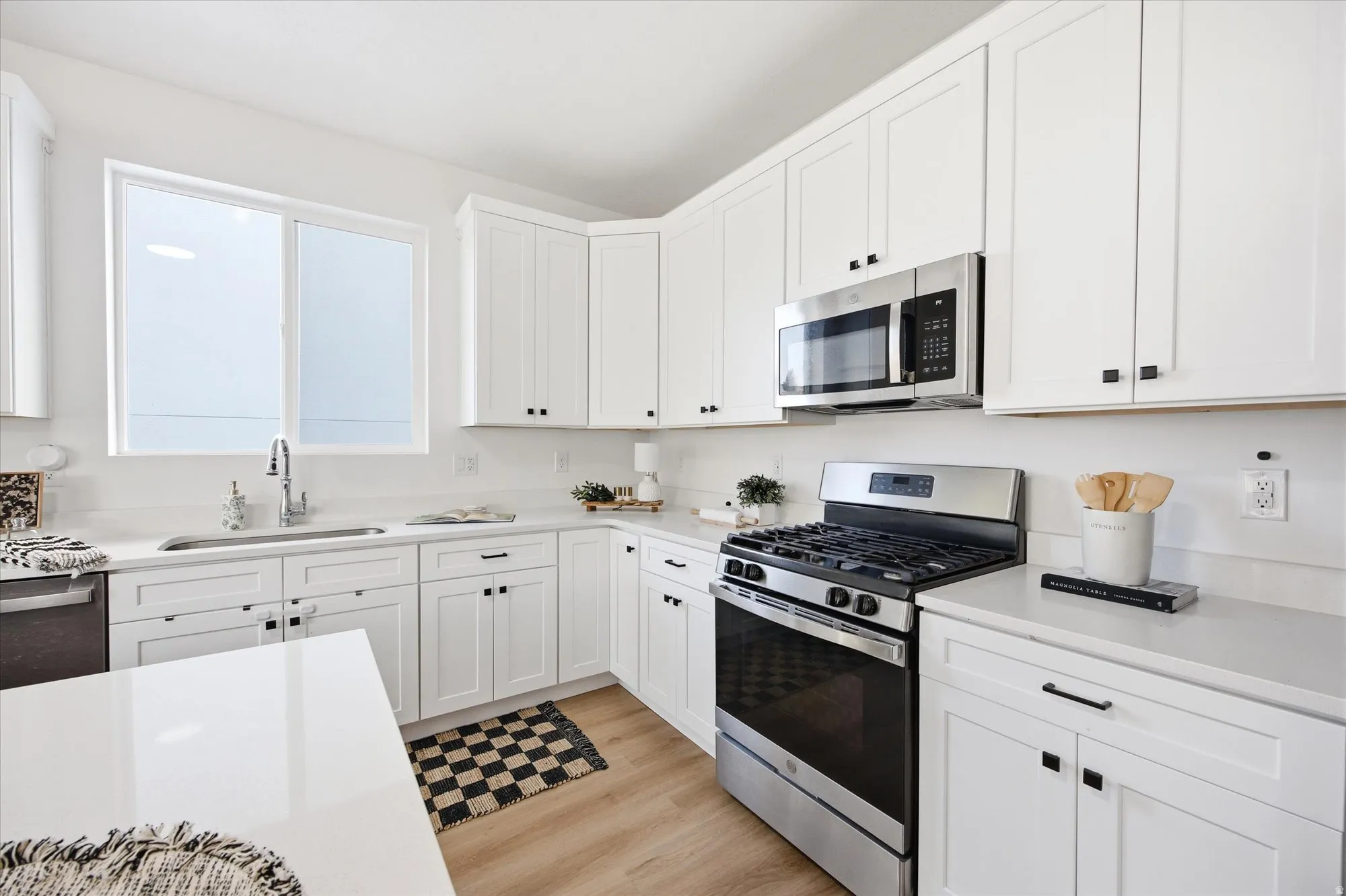 Kitchen featuring white cabinetry, stainless steel appliances, light-toned countertops, wood-finish flooring, and a large window