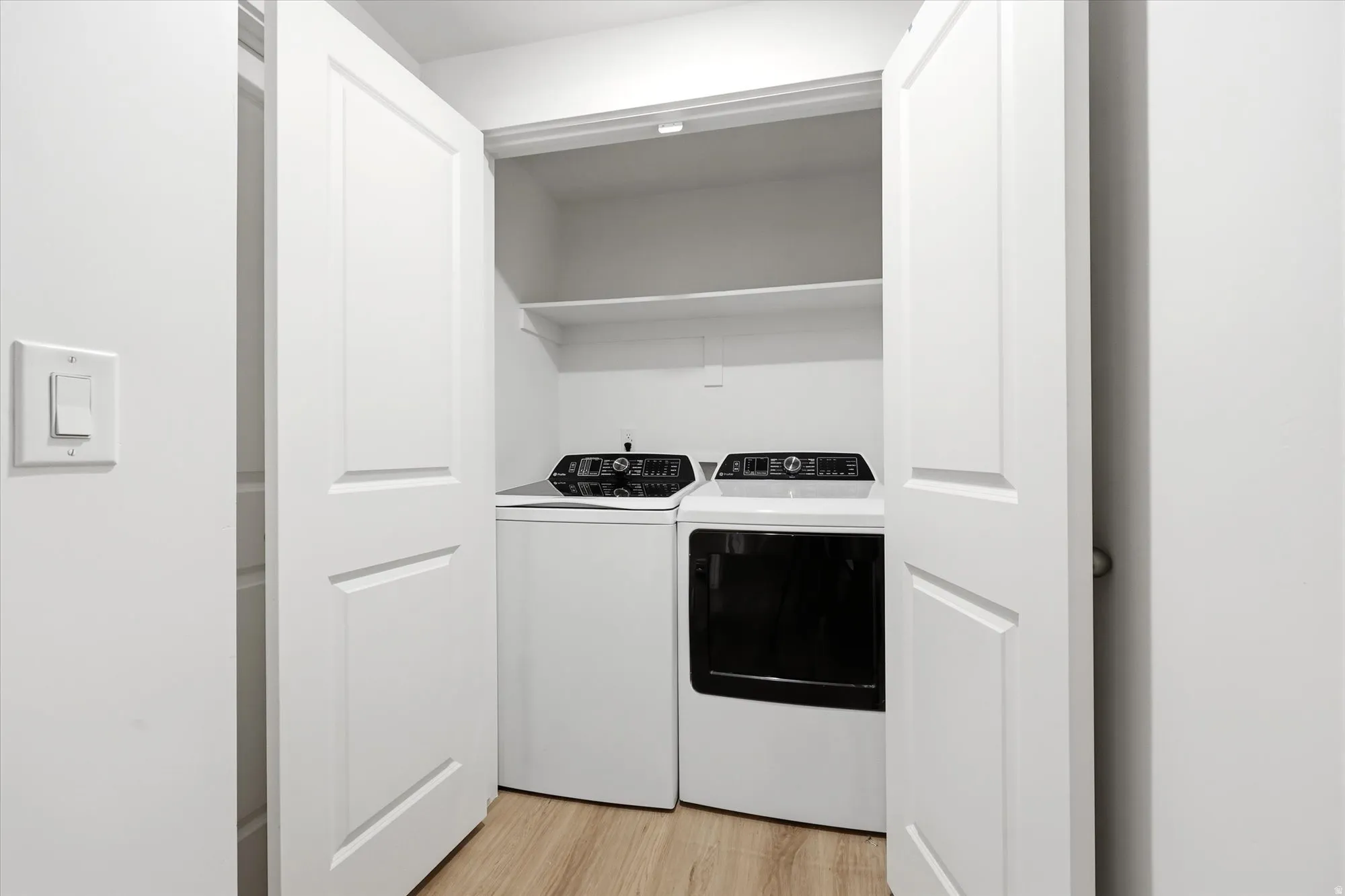 White panel doors enclose a laundry area with light wood-finish flooring and integrated shelving