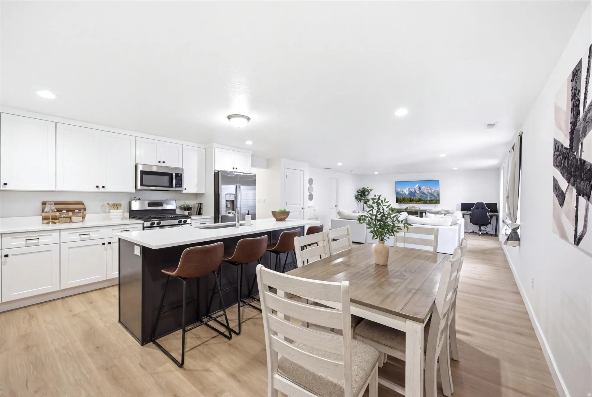 Modern kitchen featuring white shaker cabinets, stainless steel appliances, a dark-toned island with a white countertop, and wood-finish flooring
