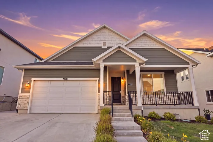 Siding exterior with stone accents, covered front porch, integrated two-car garage, and concrete driveway