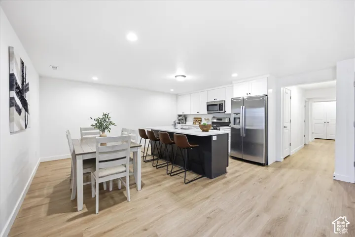 Open-concept living area featuring wood-finish flooring, recessed lighting, and a kitchen with stainless steel appliances, white cabinetry, and a central island with countertop seating