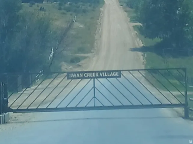 Property Entrance. Displaying a gate with the inscription "SWAN CREEK VILLAGE" and a dirt road extending beyond it