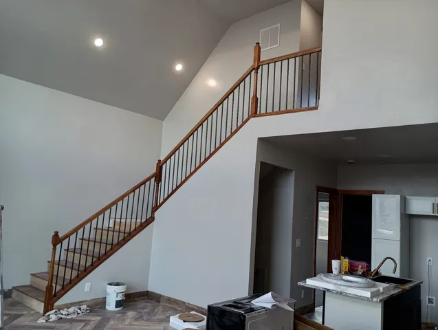 Vaulted ceiling with recessed lighting, wood-finish flooring in a herringbone pattern, and a staircase with wood newel posts and metal balusters