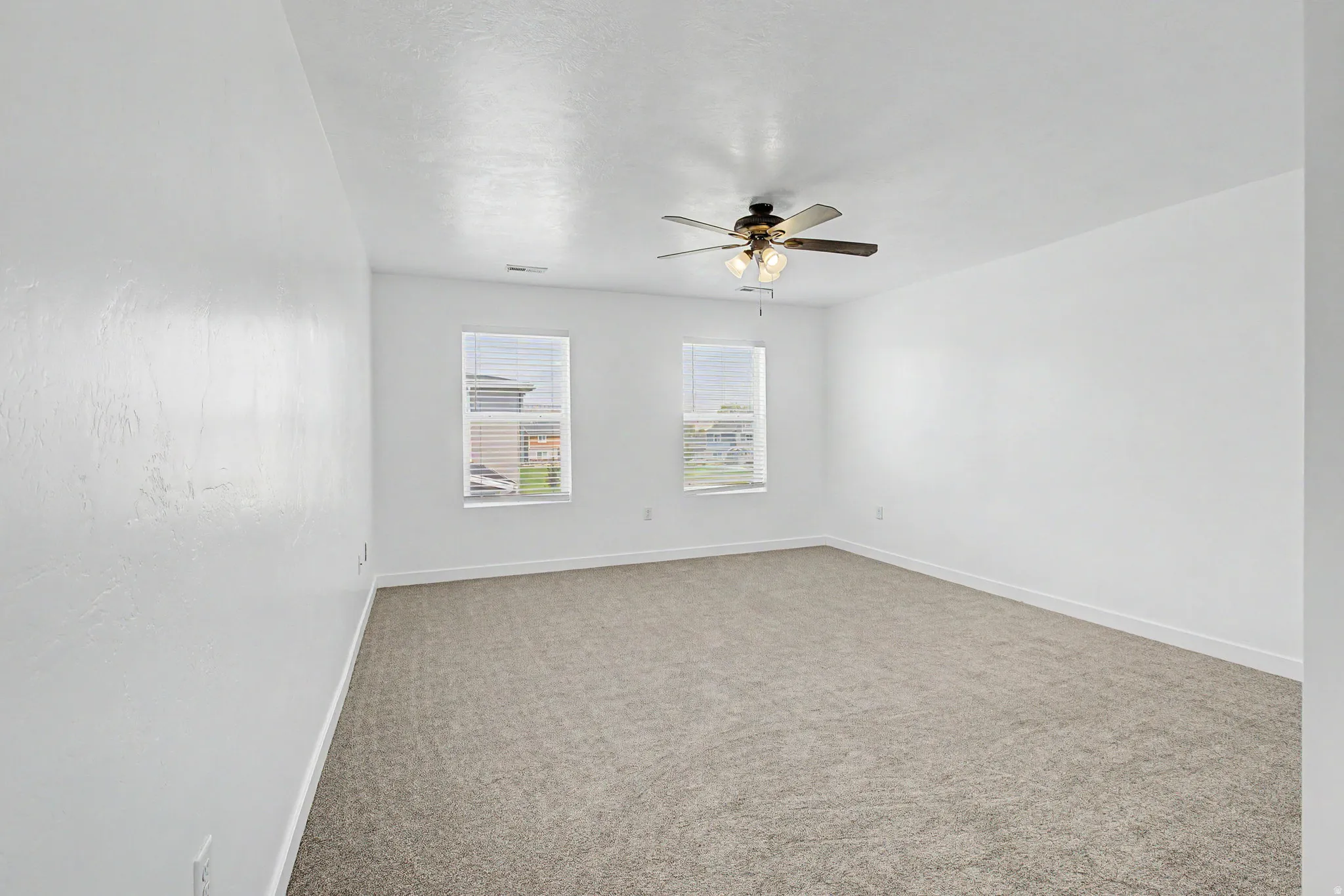 White walls, neutral carpet flooring, two windows with blinds, and a ceiling fan with integrated lighting