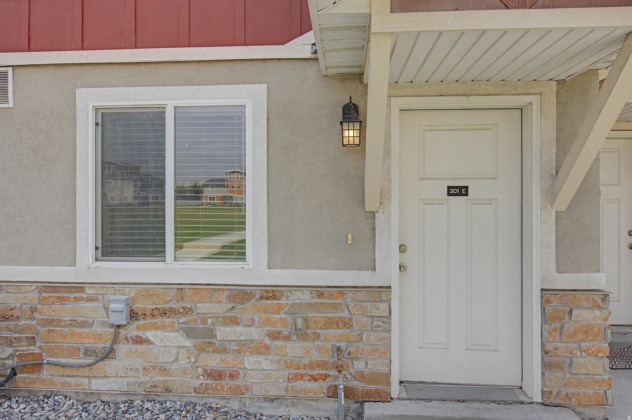 Exterior features include a paneled entry door, a single-hung window, wall-mounted exterior lighting, and a stone facade