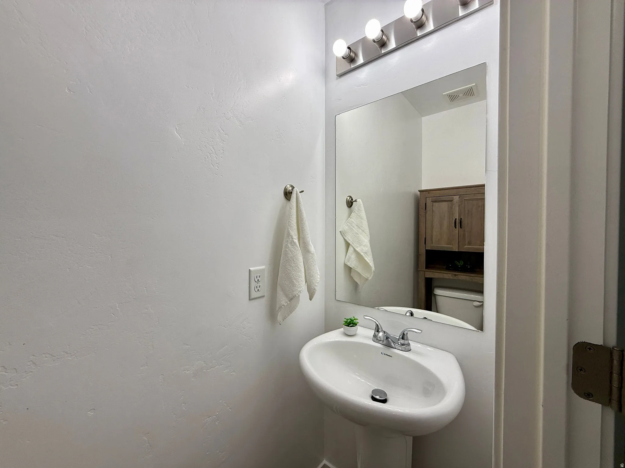 Pedestal sink with a chrome faucet, large rectangular mirror, and a four-bulb vanity light fixture