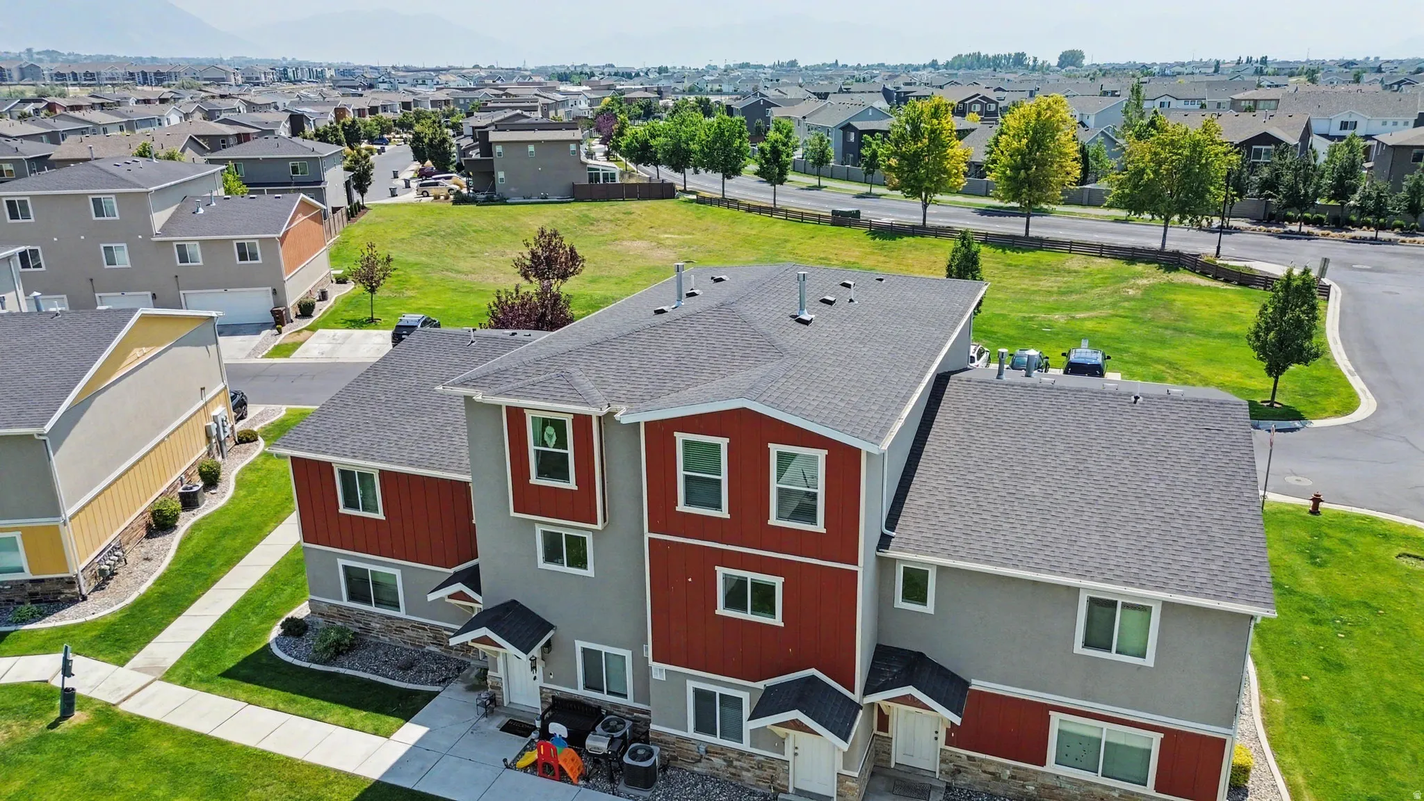 Townhome exterior featuring gray siding, red accent panels, covered entryways, and a shingled roof