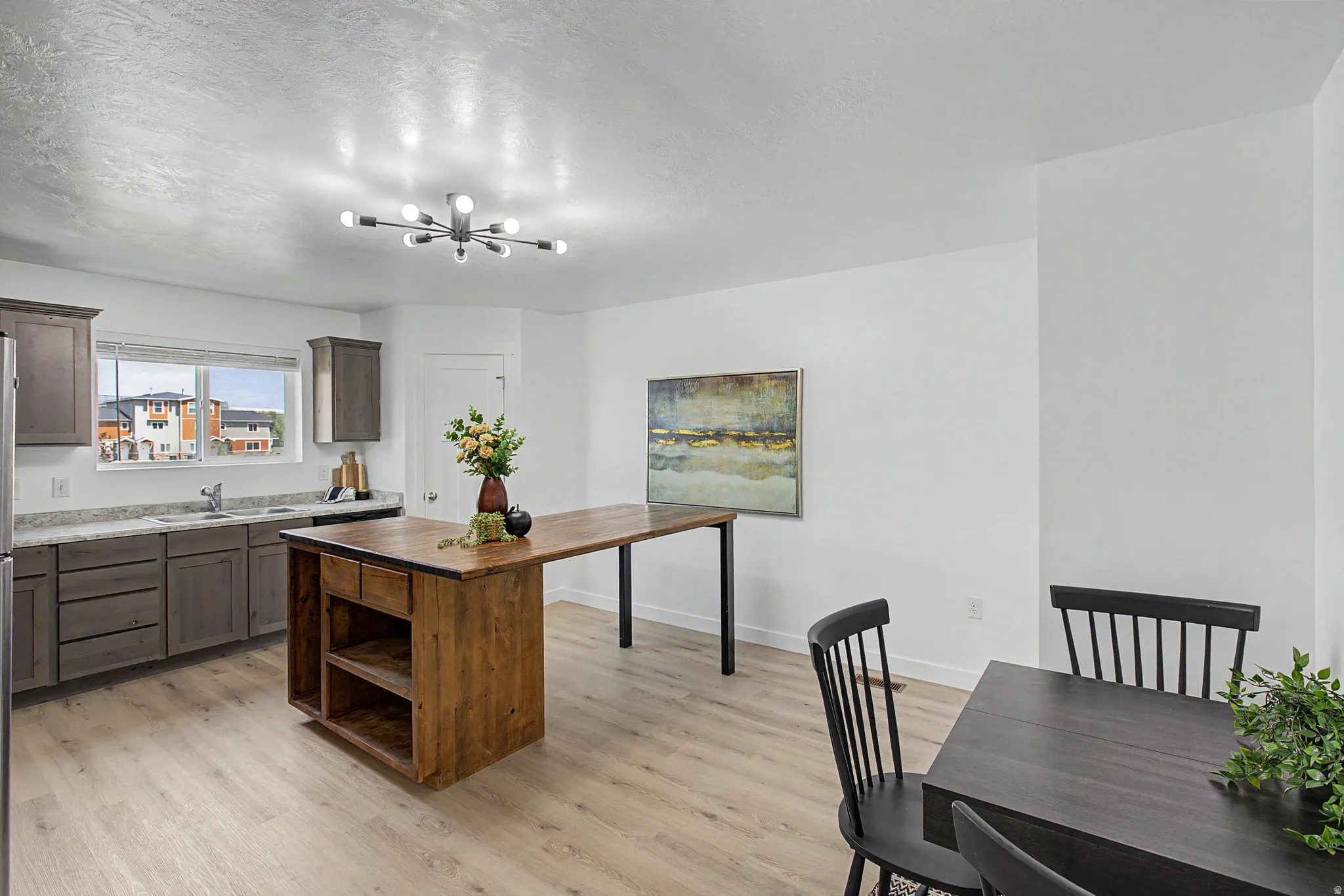 Kitchen featuring light wood-finish flooring, grey cabinetry, light-toned countertops, a stainless steel sink, and a modern sputnik-style ceiling fixture