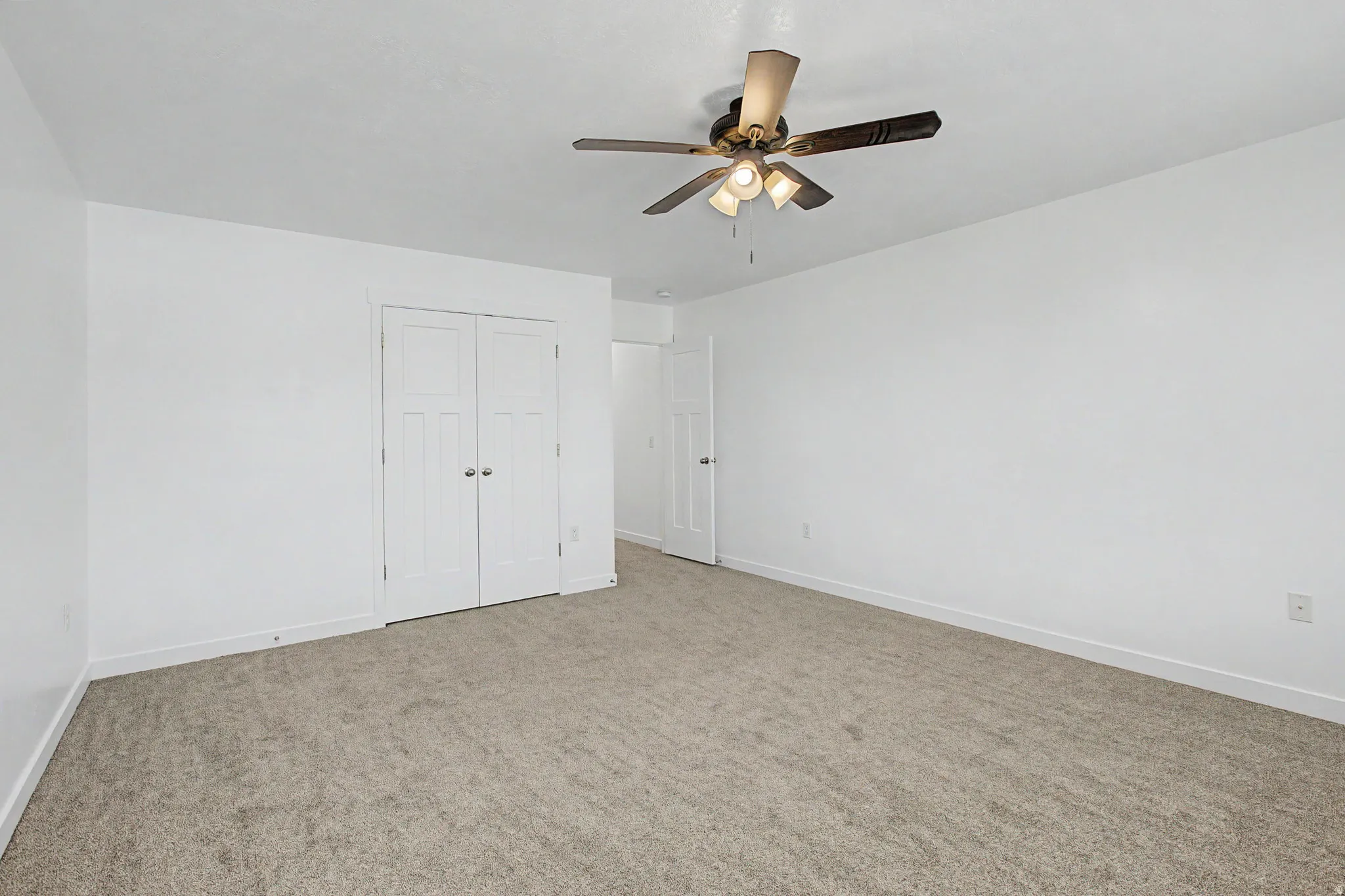 Neutral-toned carpeting with white walls, a ceiling fan with integrated lighting, and a white paneled door