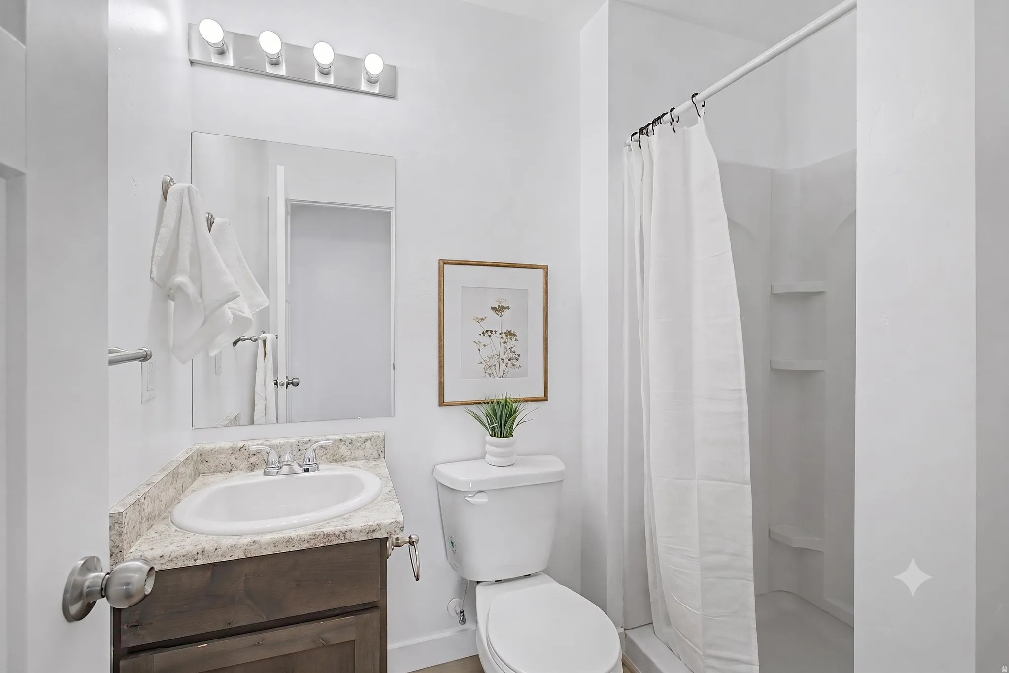 White interior walls, shower with integrated shelving, corner vanity with a speckled countertop, and a contemporary light fixture