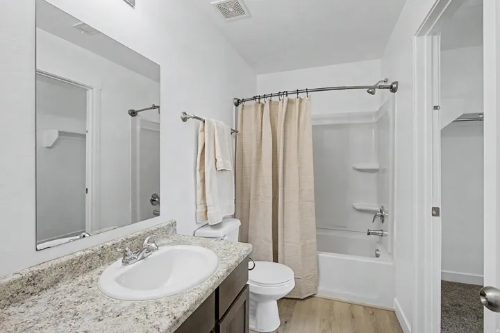 Bathroom featuring a white bathtub with an integrated shower, a white oval sink, a light-toned countertop, a rectangular mirror, and wood-finish flooring
