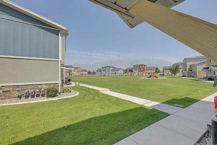 Expansive green space featuring a paved walkway, distant playground equipment, and mountain scenery from the front door