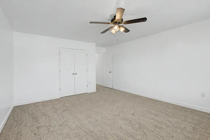 Neutral-toned carpeting with white walls, a ceiling fan with integrated lighting, and a white paneled door