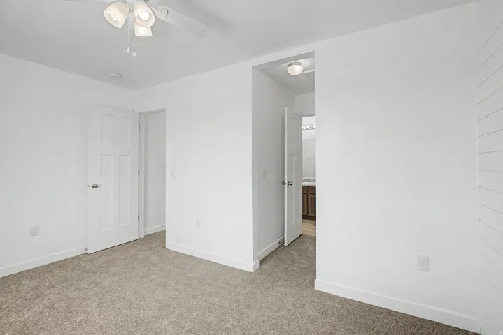 Plush carpet flooring, white walls, white paneled doors, ceiling fan with integrated lighting, and a shiplap accent wall