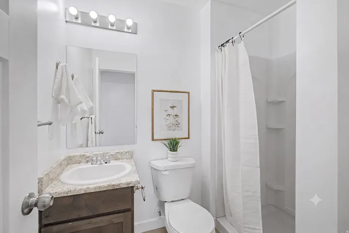 White interior walls, shower with integrated shelving, corner vanity with a speckled countertop, and a contemporary light fixture