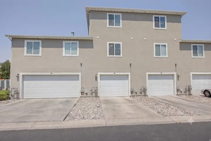 Stucco exterior with multiple white-framed windows, individual garage doors, and concrete driveways