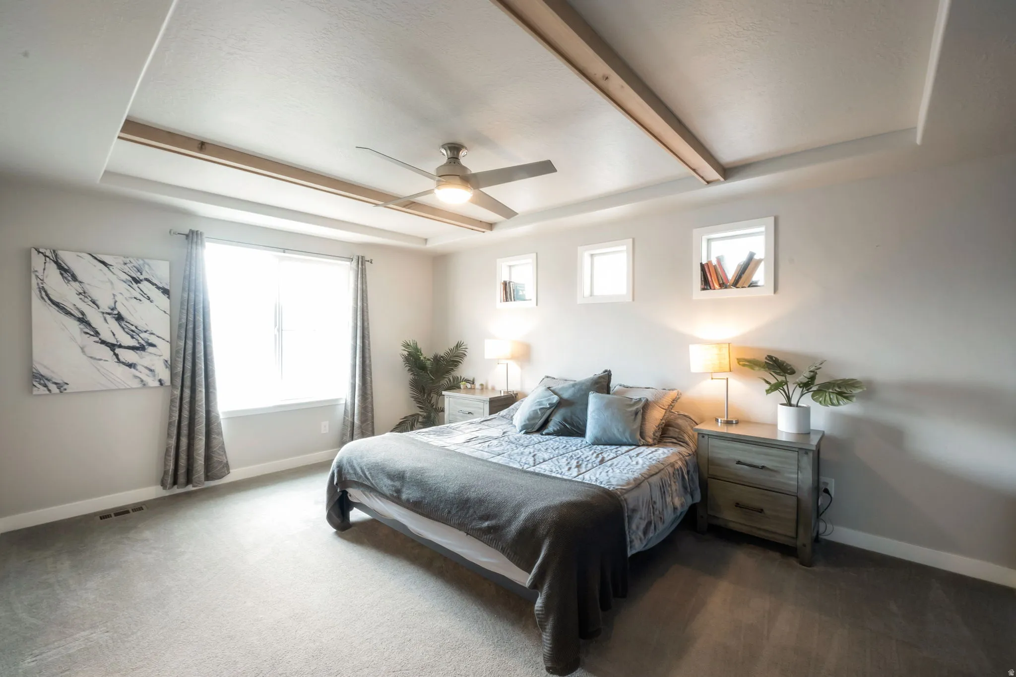 Primary bedroom with recessed tray ceiling with wood-finish beams and a ceiling fan