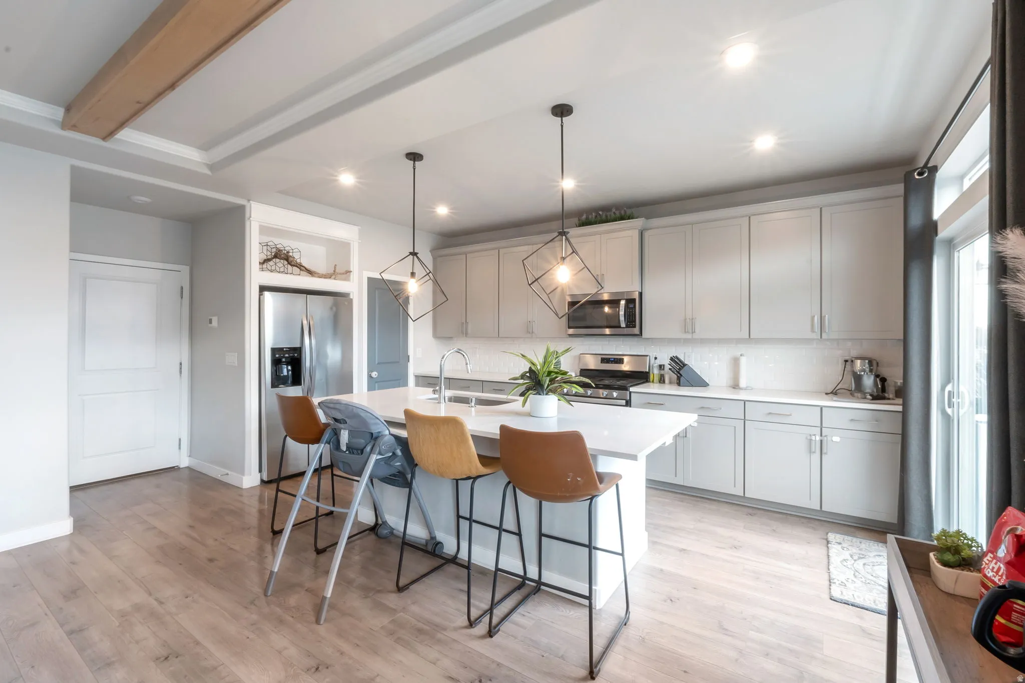 Modern kitchen and dining area featuring white cabinetry with integrated stainless steel appliances, a waterfall-edge white island with seating, pendant lighting, and laminate flooring throughout