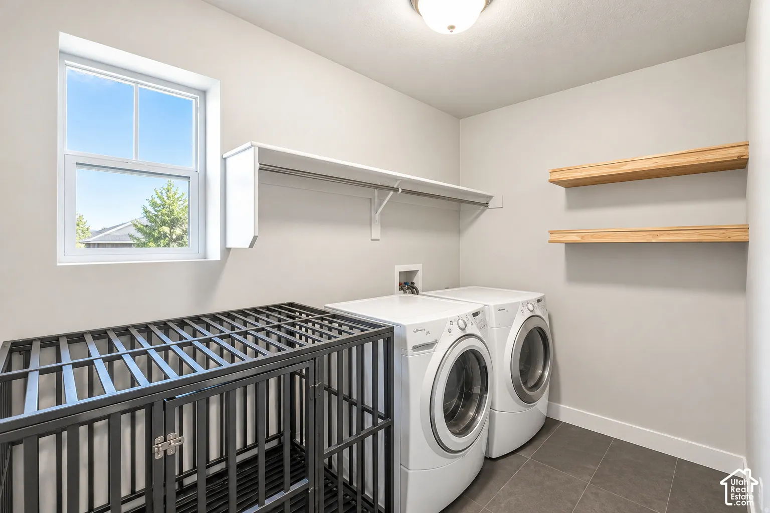 Recessed laundry area featuring tile flooring, white shelving, and natural wood-finish floating shelves