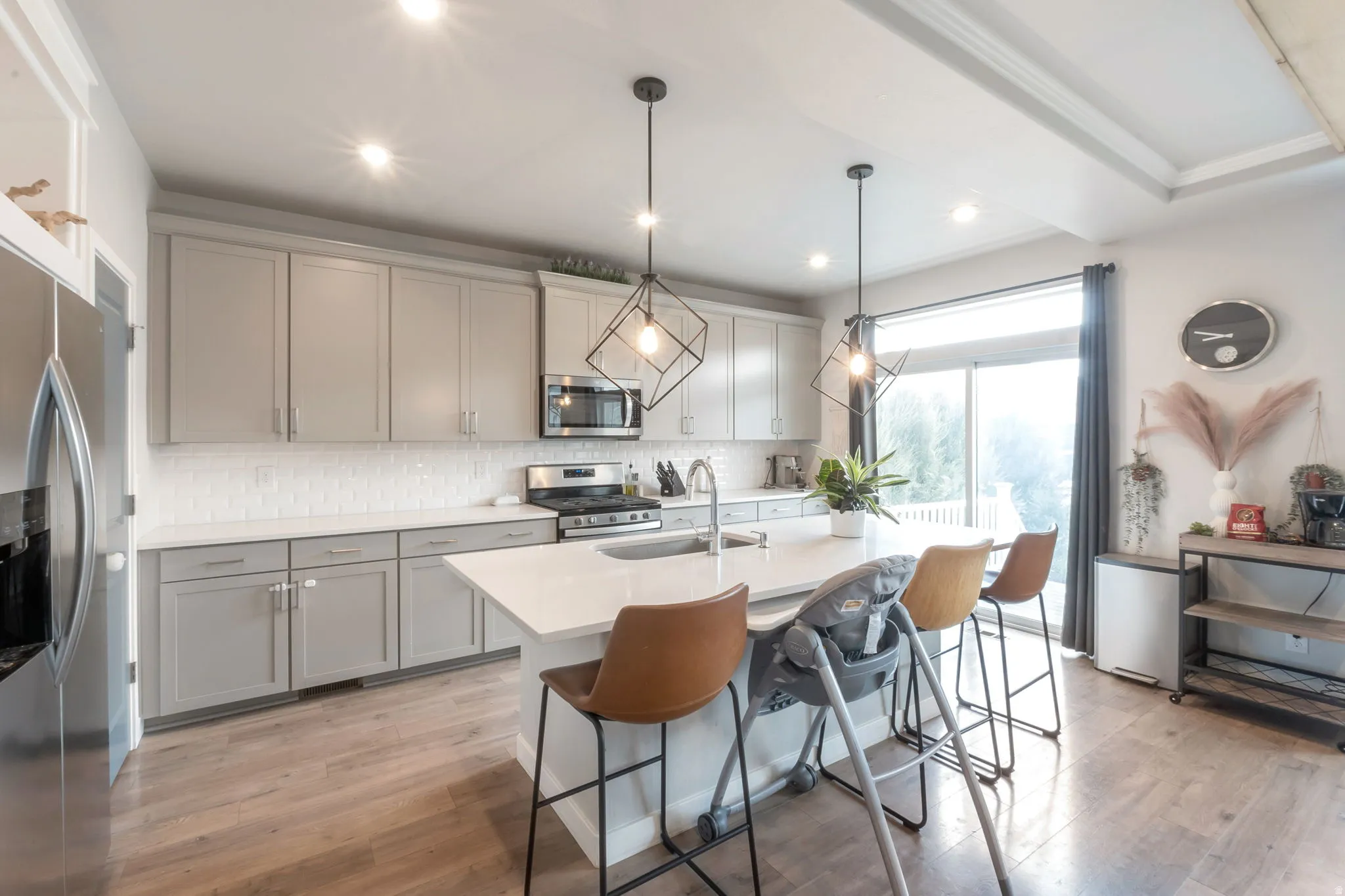 Modern kitchen featuring light gray cabinetry, white subway tile backsplash, stainless steel appliances, a center island with countertop seating, laminate  flooring