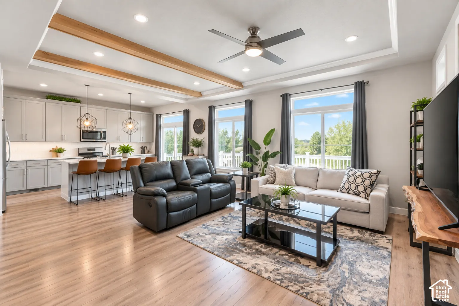 Open concept living area with wood-finish flooring, a kitchen island with seating, pendant lighting, recessed ceiling lighting, and a tray ceiling with exposed wood beams