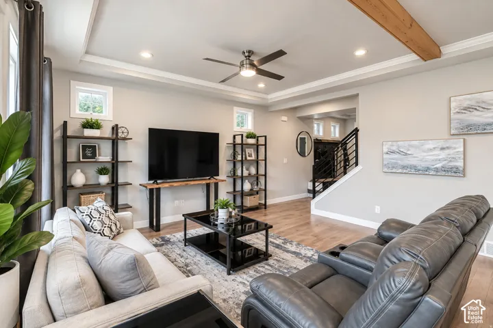 Tray ceiling with crown molding, recessed lighting, wood-finish flooring, exposed wood beam accent, and a modern ceiling fan