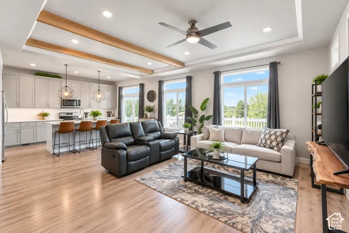 Open concept living area with wood-finish flooring, a kitchen island with seating, pendant lighting, recessed ceiling lighting, and a tray ceiling with exposed wood beams