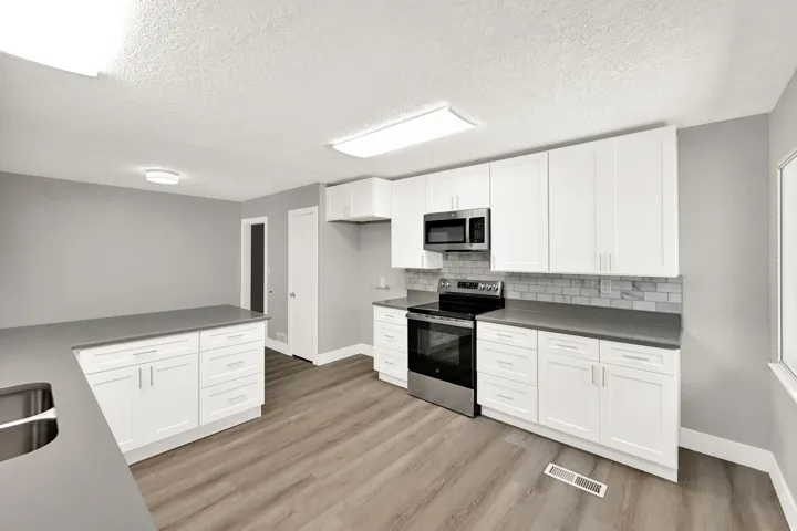 Modern kitchen featuring white shaker cabinetry, stainless steel appliances, dark countertops, a subway tile backsplash, and wood-finish flooring