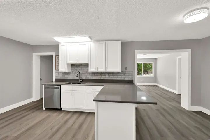 Open-concept kitchen with white shaker cabinetry, dark countertops, a subway tile backsplash, and wood-finish flooring