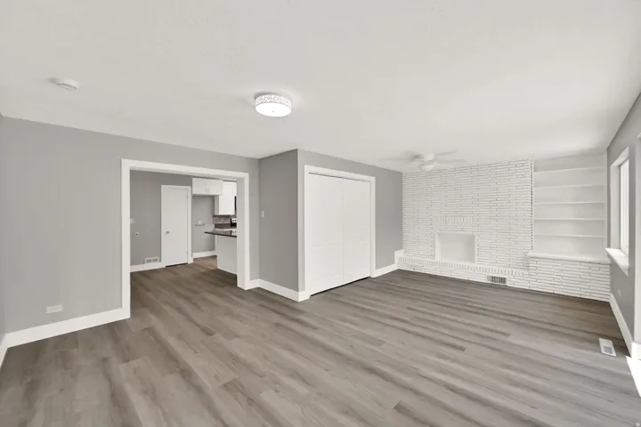 Wood-finish flooring throughout, white painted brick fireplace, built-in shelving, white bi-fold closet doors, and recessed lighting