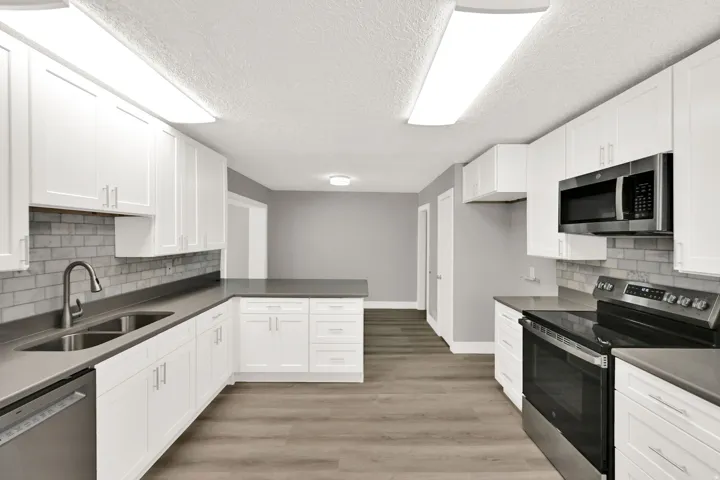 U-shaped kitchen featuring white shaker cabinetry, gray countertops, stainless steel appliances, a subway tile backsplash, and wood-finish flooring