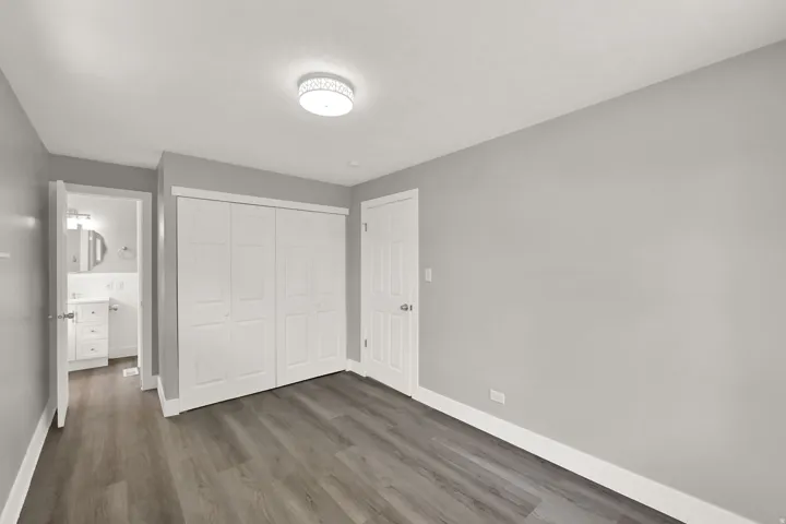 Wood-finish flooring, white bi-fold closet doors, white interior door, and a flush mount ceiling light fixture