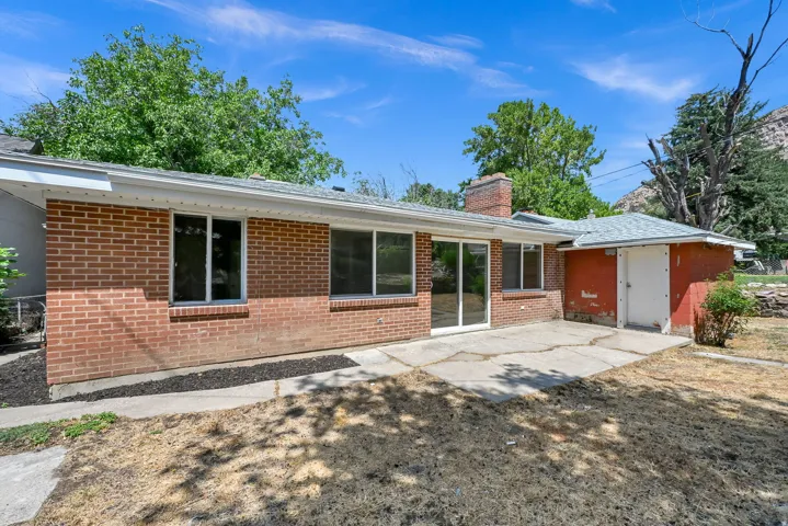 Brick exterior with multiple windows and sliding glass doors, concrete patio, and attached storage structure