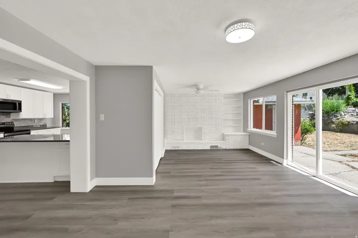 Expansive room featuring wood-finish flooring, a white brick fireplace, built-in shelving, and sliding glass doors