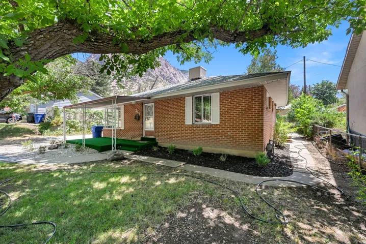 Brick exterior with white window shutters and a covered front porch featuring artificial turf
