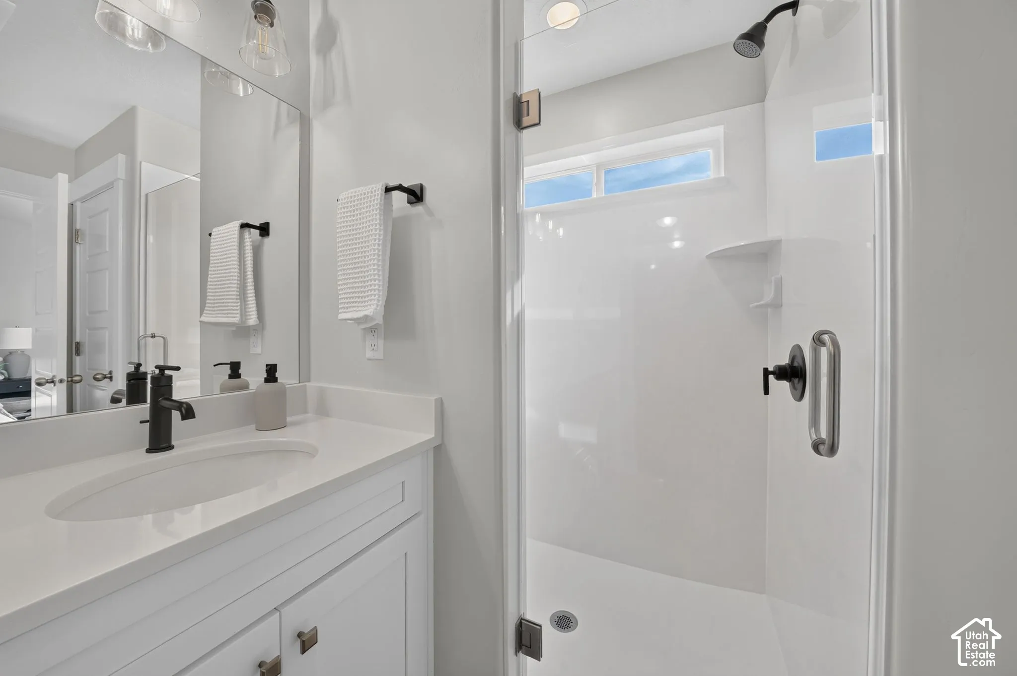 Vanity with a single undermount sink and dark bronze faucet, framed mirror, and glass-enclosed shower with a dark bronze showerhead and a horizontal window