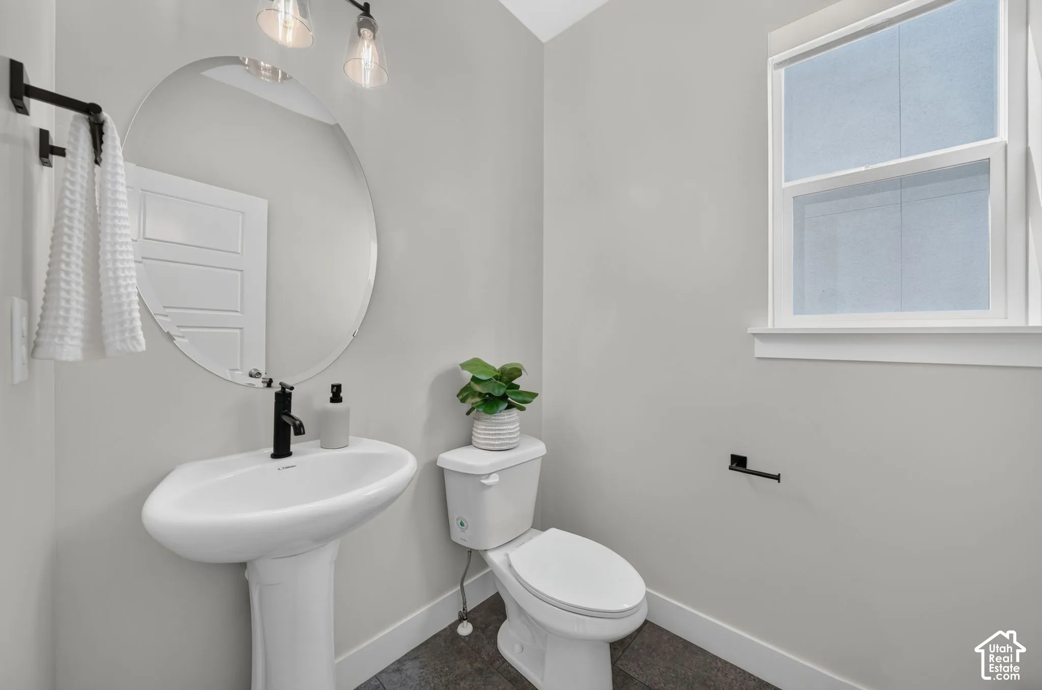 White pedestal sink with a matte black faucet, oval wall-mounted mirror, and overhead track lighting